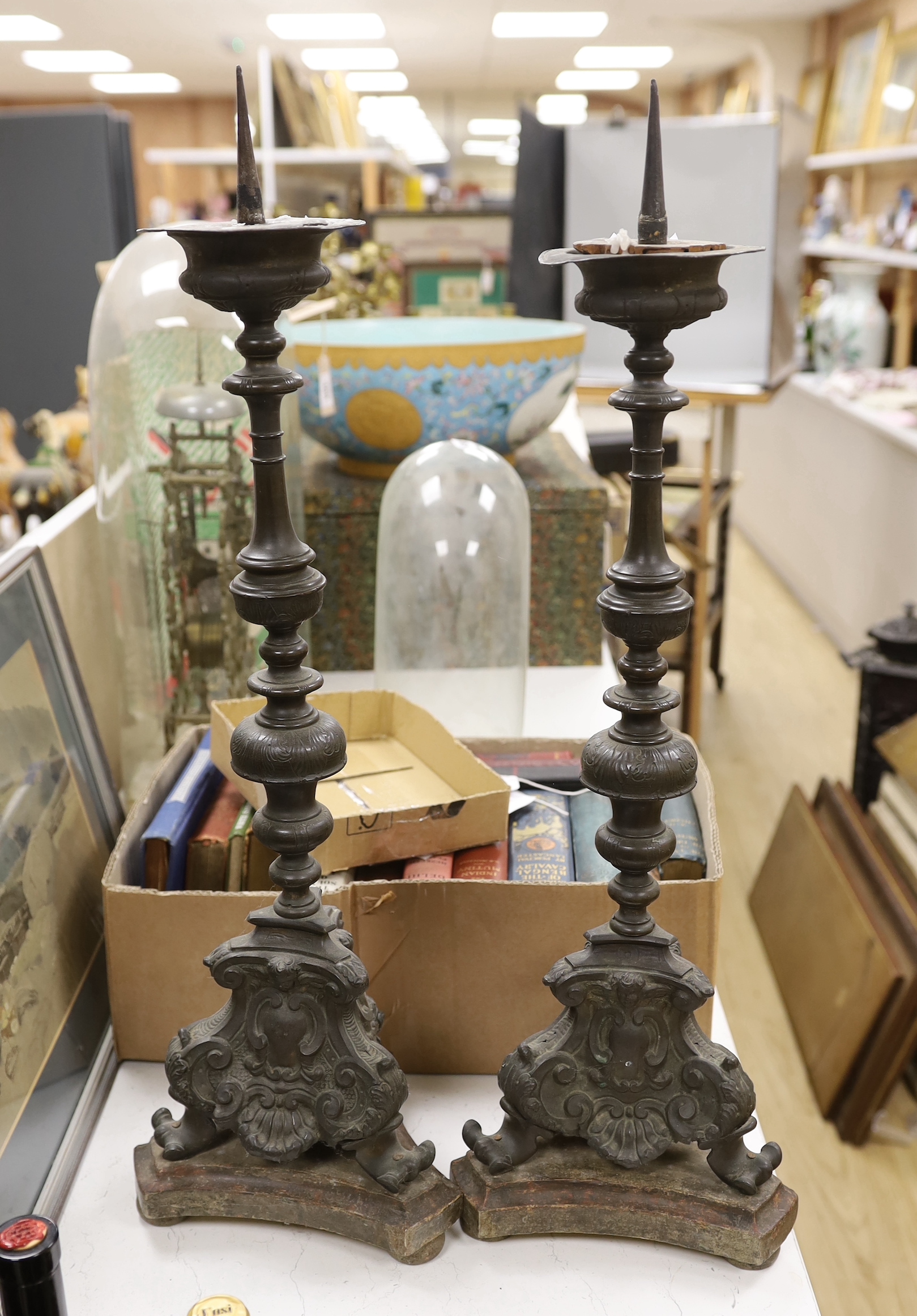 A pair of late 17th / 18th century Italian altar pricket candlesticks of sheet brass, each with foliate knopped baluster stem with shell, putto mask and cartouche bases, above wooded bases, 69cm